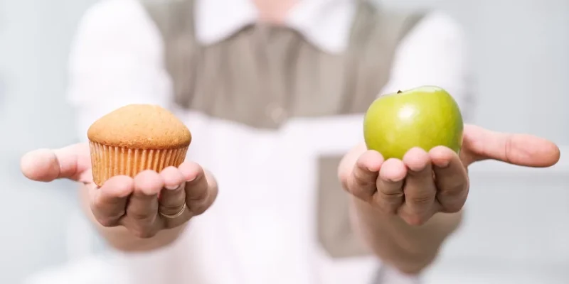 A person holding an apple and cupcake in their hands.
