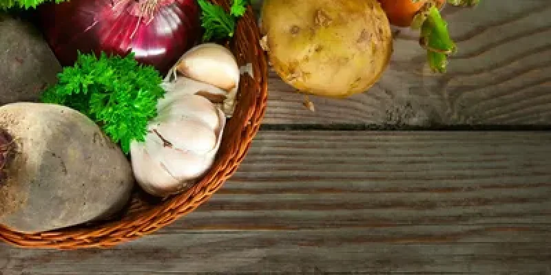 A basket of vegetables on top of a wooden table.